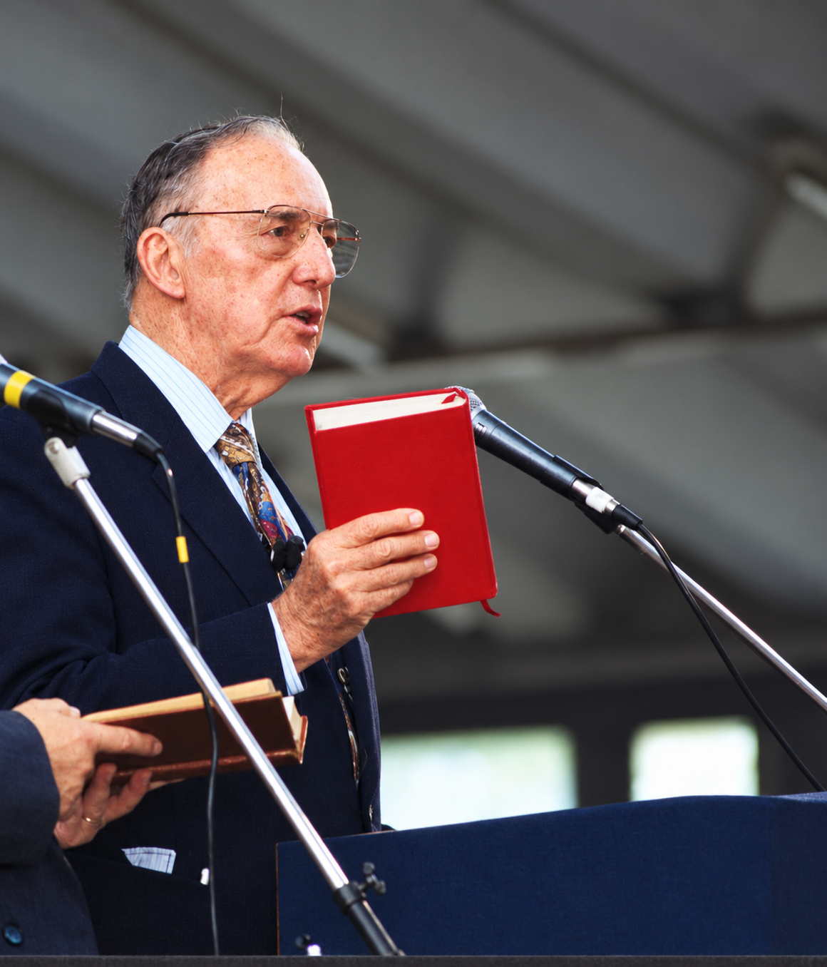 Derek Prince met een boek achter meerdere microfoons